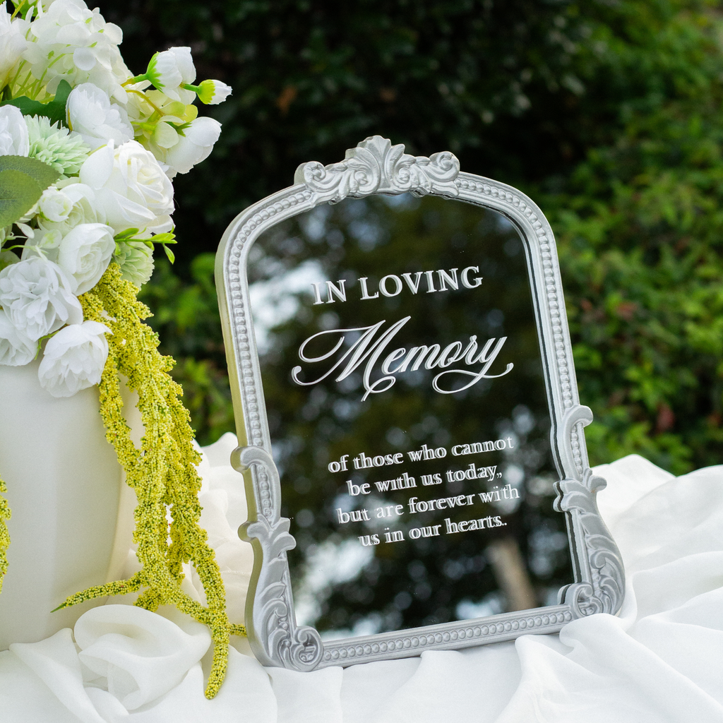 An oval freestanding mirror with a leopard-print frame and cursive text reading 'the Love Stories Before Our's' displayed on a white tablecloth beside gold picture frames and white flowers.